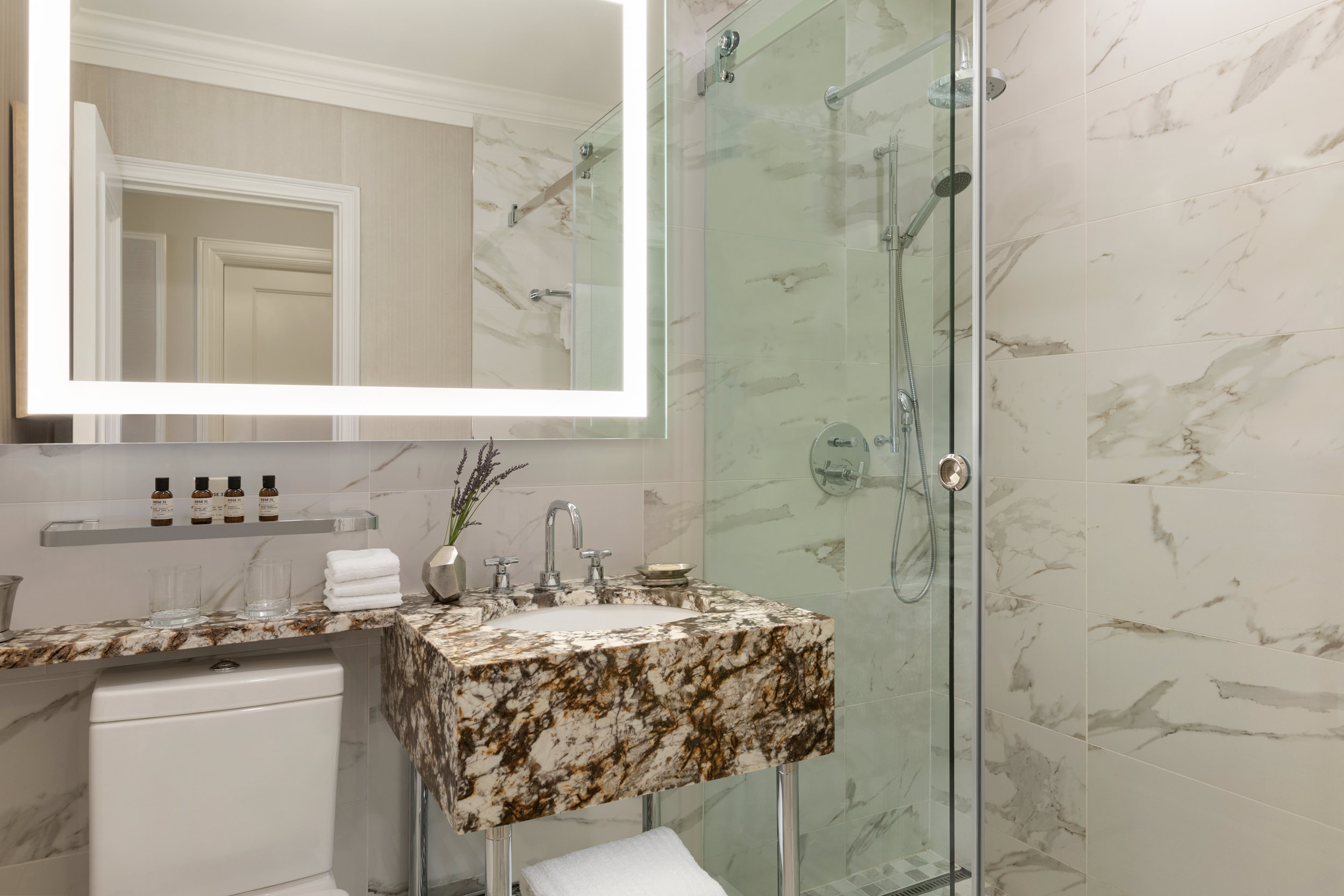 A marble bathroom sink basin next to a glass shower