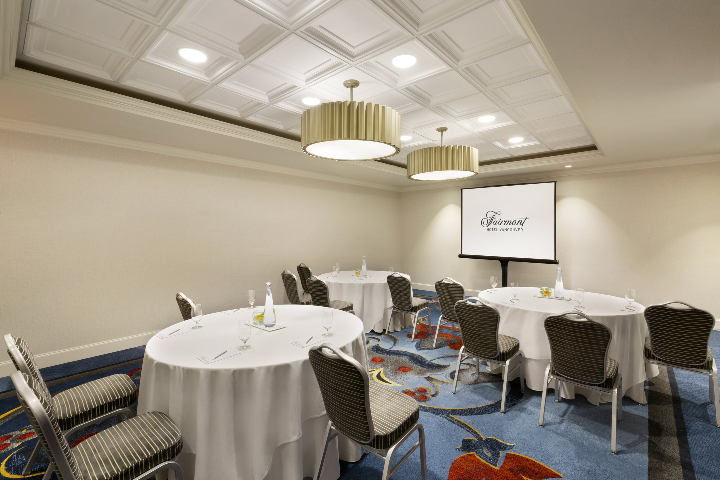 three tables covered with cloths with chairs facing the back of the room with a projector screen