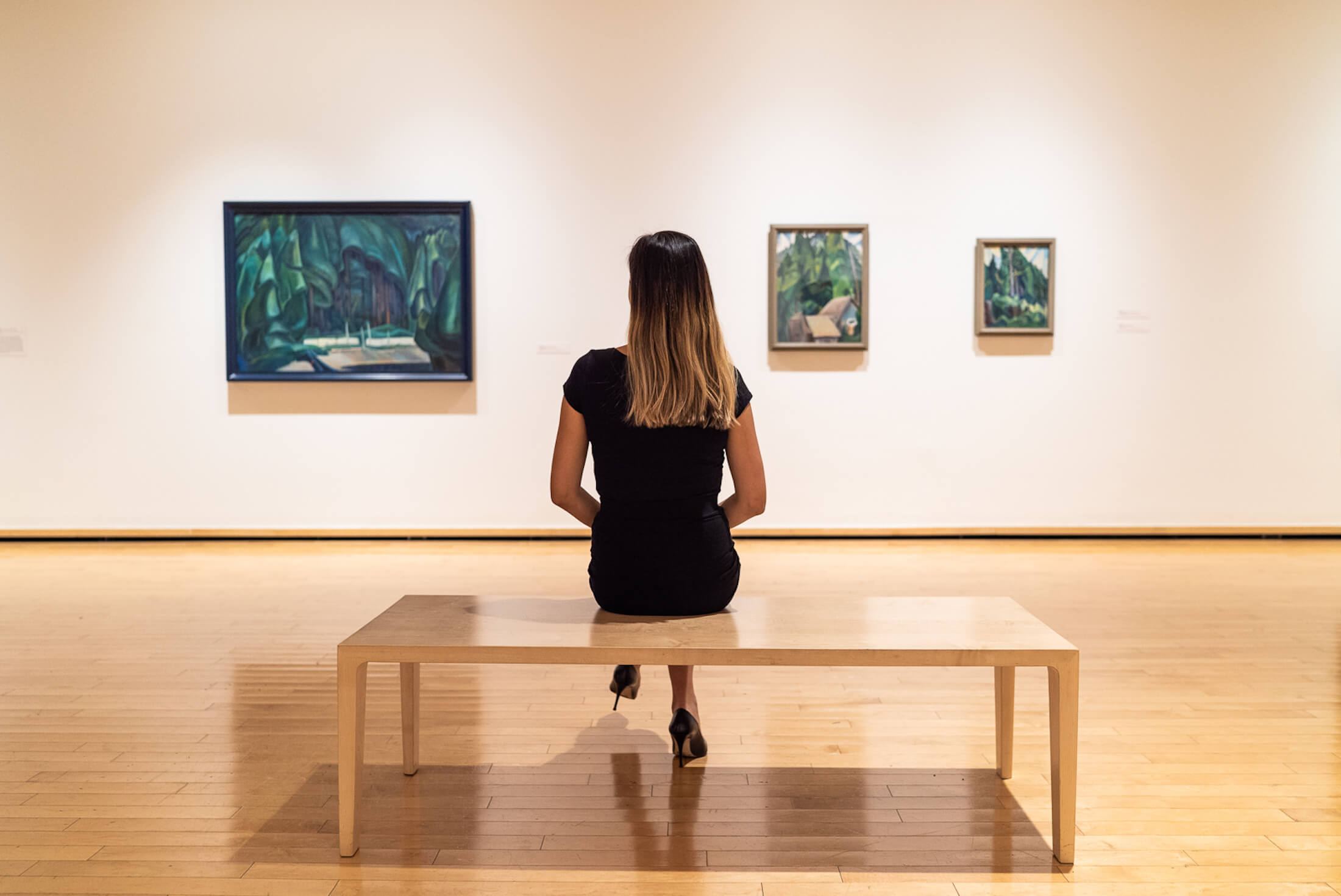 A woman sitting on a wooden bench in an art gallery