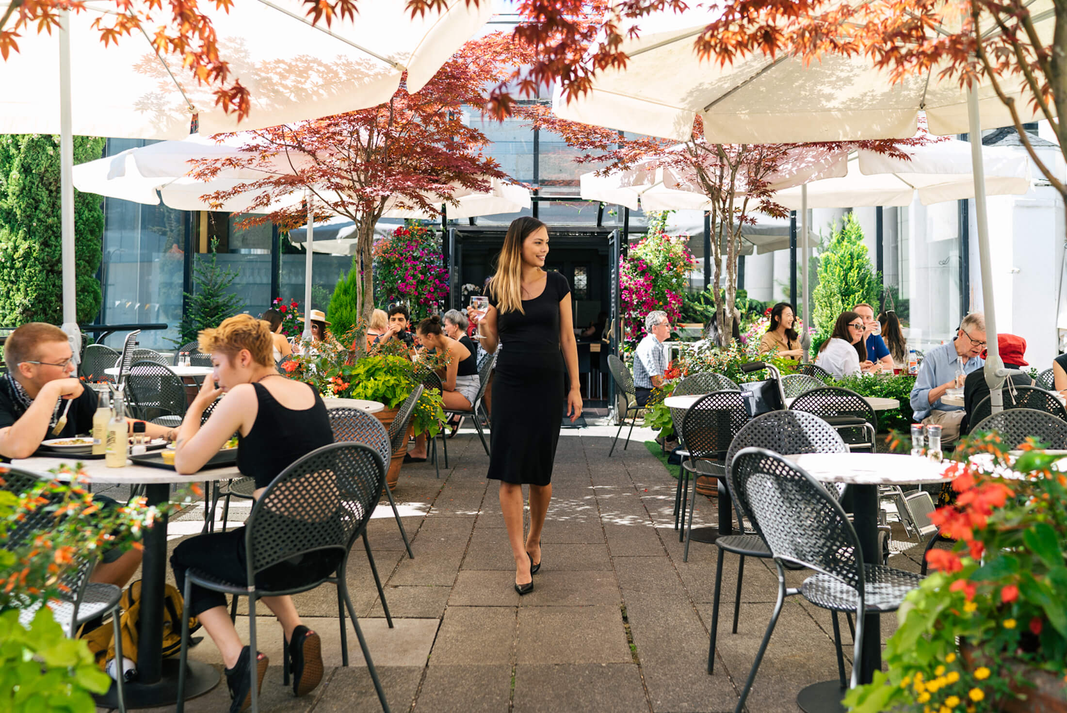 A woman holding a glass of wine and walking through an outdoor dining area