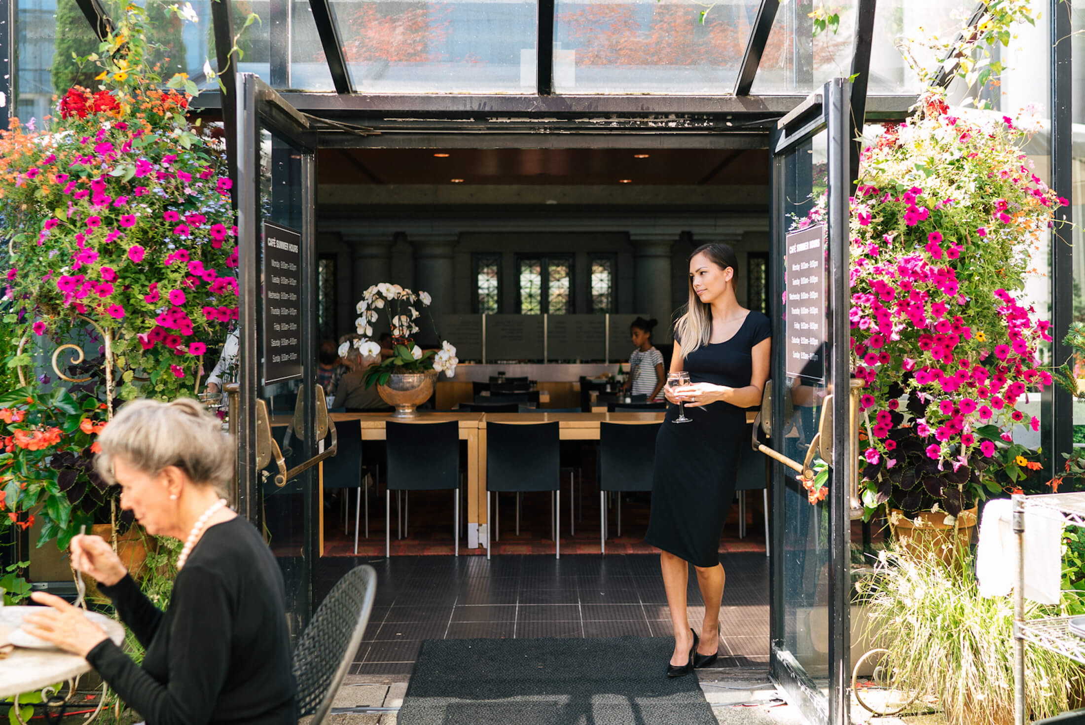 A woman holding a glass of wine standing in the door of an outdoor patio of a restaurant