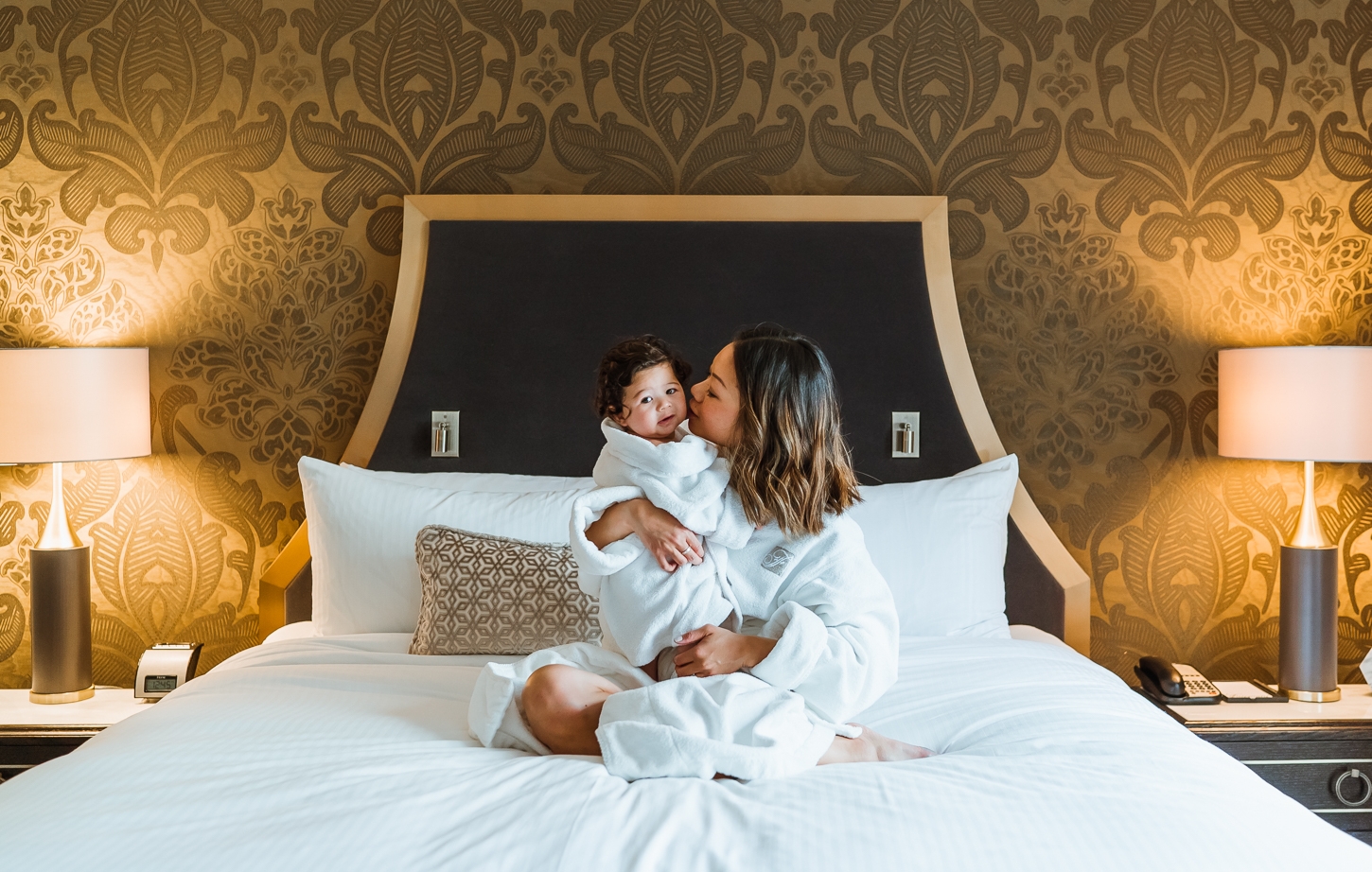 Mother and cute baby in robes on plush bed at Fairmont Hotel Vancouver