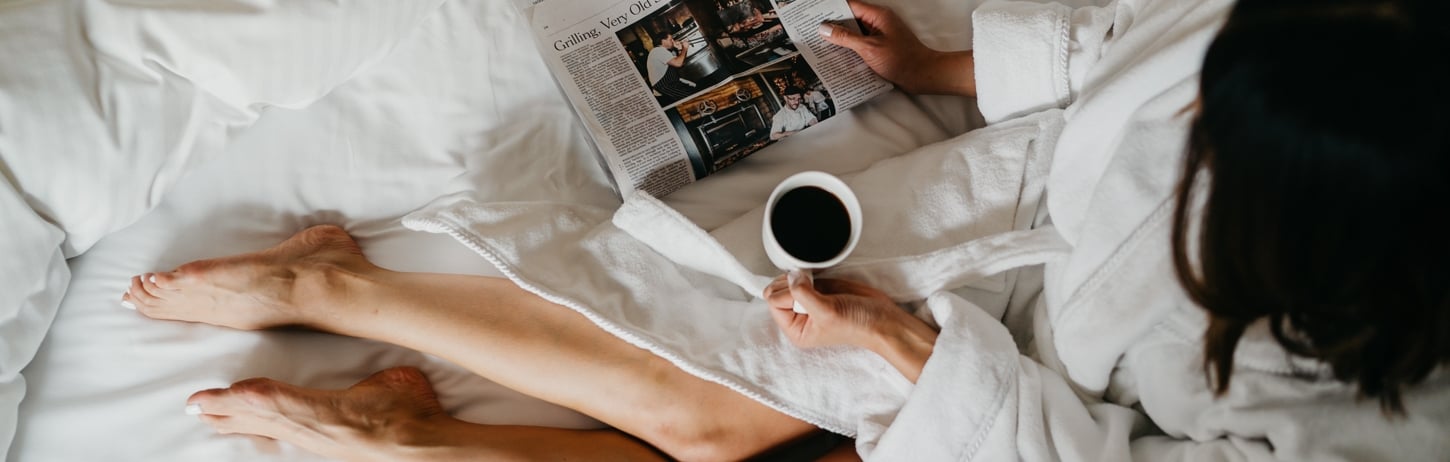 Woman relaxing in plush robe drinking a coffee and reading the paper at Fairmont Hotel Vancouver