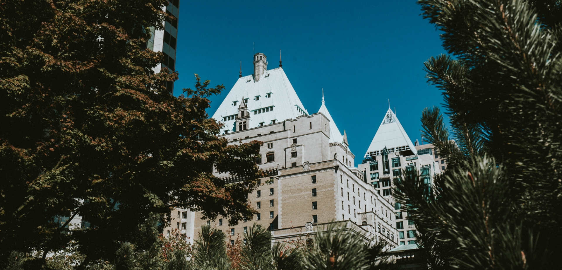 View of Fairmont Hotel Vancouver through trees on sunny day