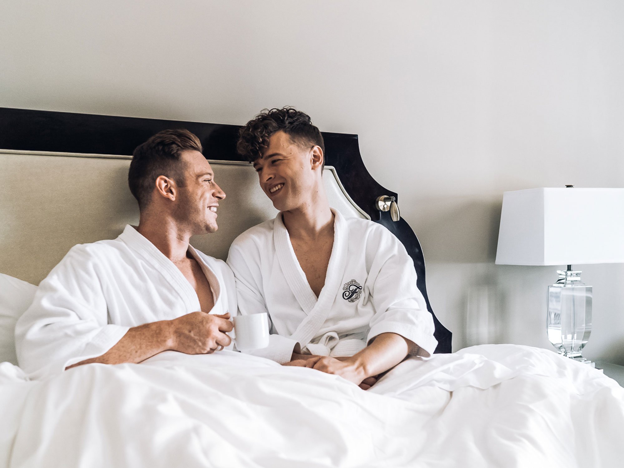 Gay couple drinking coffee in plush bed at Fairmont Hotel Vancouver