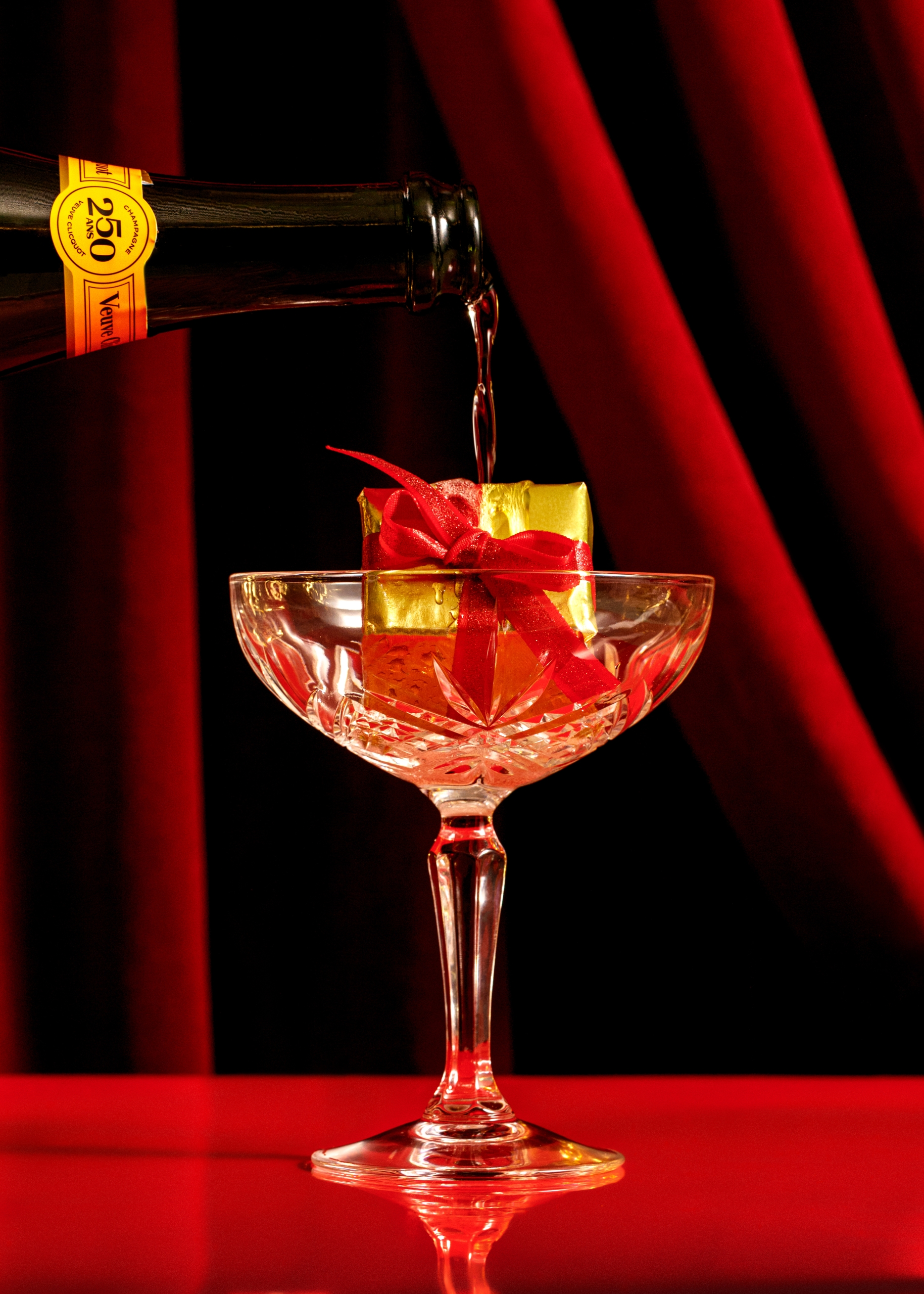 Coupe glass with gift inside in front of red velvet curtain at Kringle's Holiday Pop-Up Bar at Fairmont Hotel Vancouver