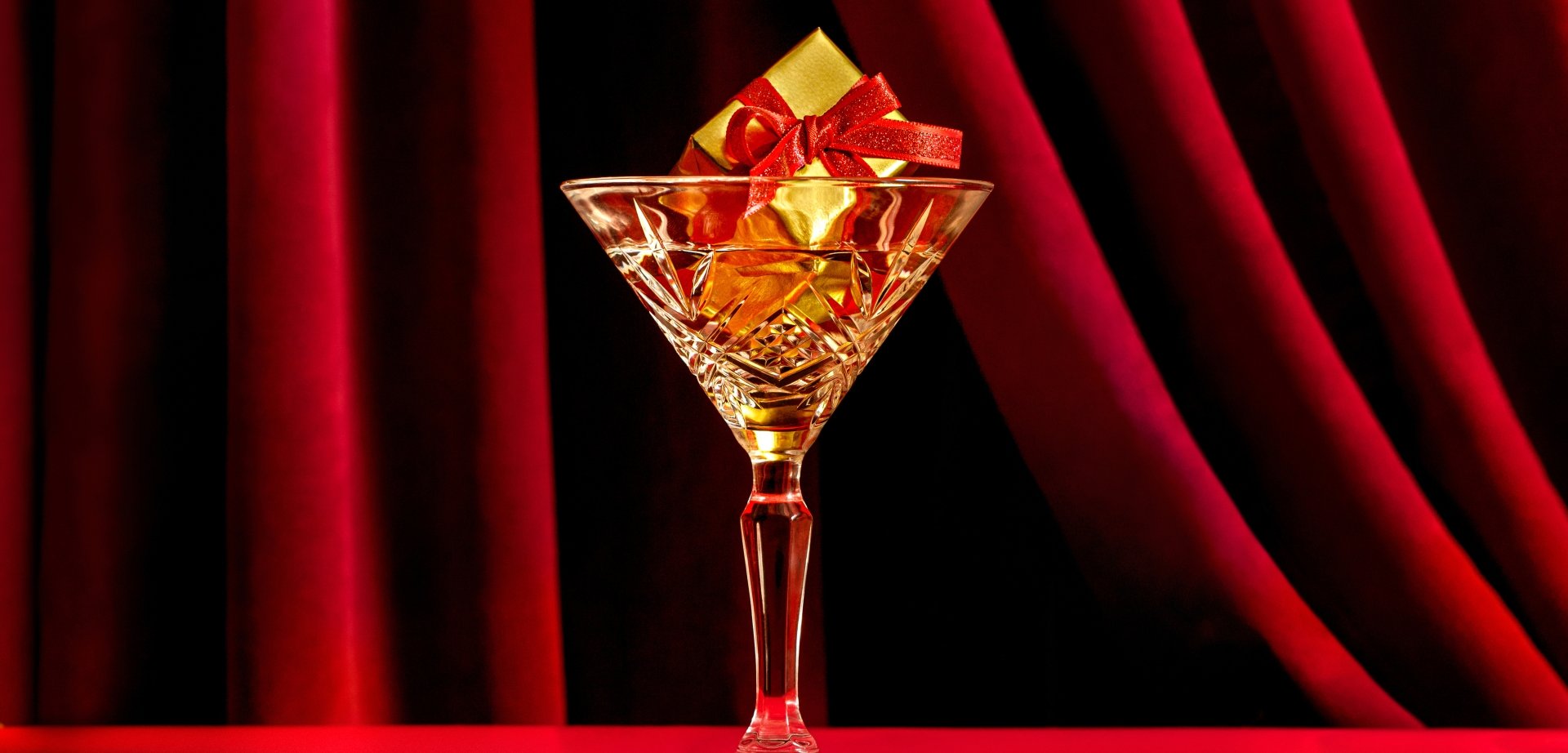 Martini glass with gift inside in front of red velvet curtain at Kringle's Holiday Pop-Up Bar at Fairmont Hotel Vancouver