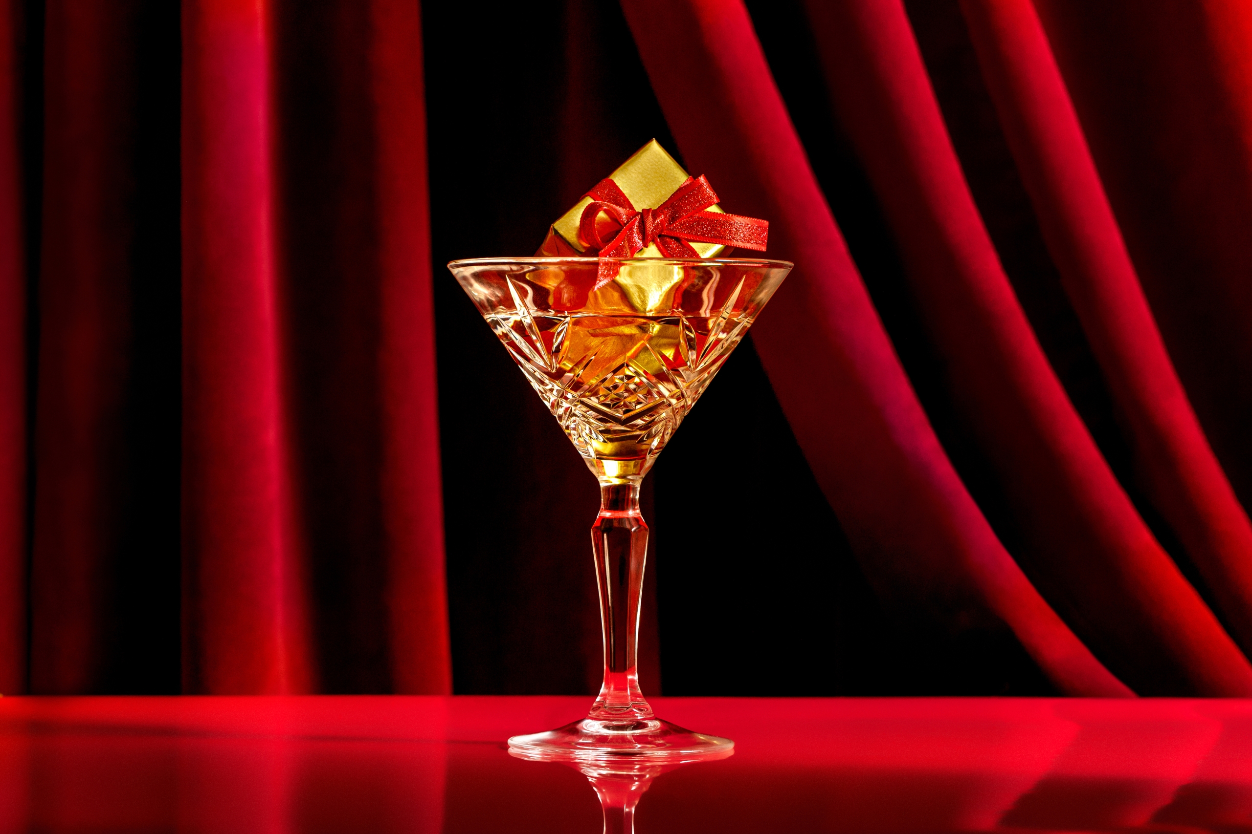Martini glass with gift inside in front of red velvet curtain at Kringle's Holiday Pop-Up Bar at Fairmont Hotel Vancouver